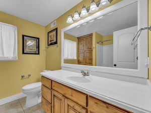 Full bathroom with vanity, tile patterned floors, toilet, baseboards, and a shower