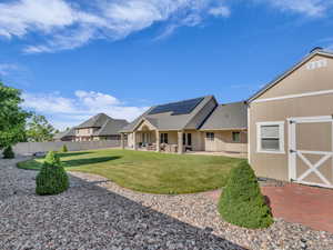 Back of house with solar panels, a patio area, and roof with shingles