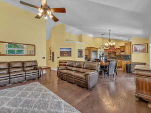 Living area featuring a ceiling fan, dark wood-type flooring, a chandelier, high vaulted ceiling, and baseboards