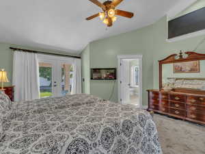 Carpeted bedroom featuring lofted ceiling, access to outside, french doors, ensuite bathroom, and a ceiling fan