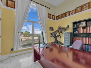 Office area featuring marble tiled flooring, plenty of natural light, a high ceiling, and baseboards