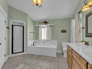 Full bath with vaulted ceiling, a garden tub, toilet, vanity, and baseboards