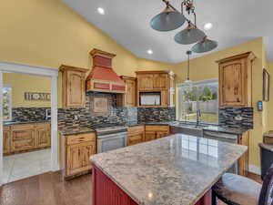 Kitchen featuring stainless steel appliances, a sink, vaulted ceiling, tasteful backsplash, and dark stone countertops