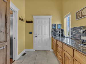 Kitchen featuring tasteful backsplash, a high ceiling, a sink, dark stone counters, and light tile patterned floors