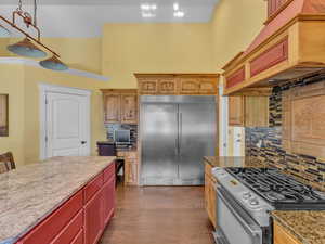 Kitchen with appliances with stainless steel finishes, a towering ceiling, backsplash, light stone countertops, and dark wood finished floors