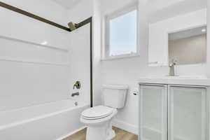 Full bathroom with wood finished floors, vanity, toilet, baseboards, and bathing tub / shower combination