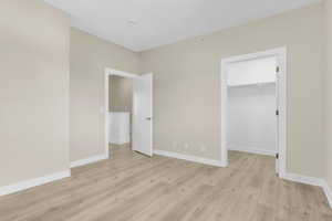 Unfurnished bedroom with light wood finished floors, a spacious closet, baseboards, and a closet