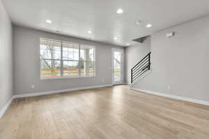 Unfurnished living room featuring stairs, recessed lighting, baseboards, and light wood-type flooring