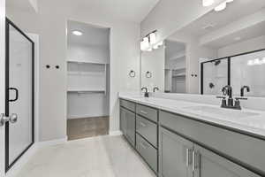 Bathroom with a walk in closet, a stall shower, double vanity, and baseboards
