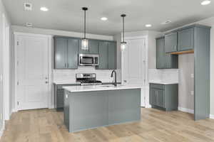 Kitchen featuring appliances with stainless steel finishes, tasteful backsplash, light countertops, a sink, and decorative light fixtures