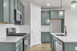 Kitchen featuring stainless steel appliances, a sink, light wood-style floors, pendant lighting, and light countertops