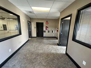 Hall with a drop ceiling, plenty of natural light, baseboards, and tile patterned floors