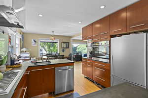 Kitchen with appliances with stainless steel finishes, a sink, ventilation hood, a peninsula, and light wood finished floors