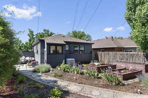 Rear view of house featuring a garden, roof with shingles, and central AC
