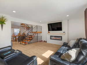 Living area featuring wood finished floors, stairway, a glass covered fireplace, and recessed lighting
