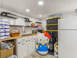 Kitchen with freestanding refrigerator, open shelves, a sink, white cabinetry, and light wood-style flooring