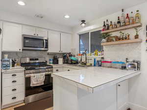 Kitchen featuring stainless steel appliances, a sink, a peninsula, white cabinetry, and decorative backsplash