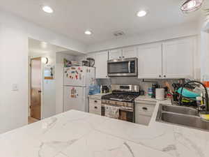 Kitchen featuring stainless steel appliances, a sink, decorative backsplash, white cabinets, and light stone countertops