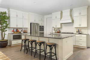 Kitchen featuring a sink, premium range hood, stainless steel appliances, dark countertops, and wood finished floors
