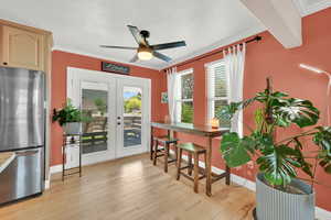 Dining space featuring french doors, a ceiling fan, crown molding, light wood-style floors, and a textured ceiling