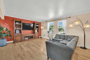 Living area with baseboards, light wood finished floors, a textured ceiling, and ornamental molding