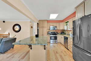 Kitchen featuring stainless steel appliances, a sink, light wood-style flooring, light stone countertops, and a kitchen island