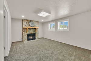 Unfurnished living room with a stone fireplace, carpet floors, a textured ceiling, recessed lighting, and baseboards