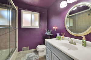 Bathroom with toilet, vanity, tile patterned flooring, enclosed tub / shower combo, and baseboards