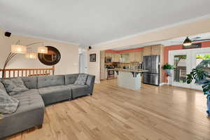 Living room with ornamental molding, light wood-style flooring, a ceiling fan, and baseboards