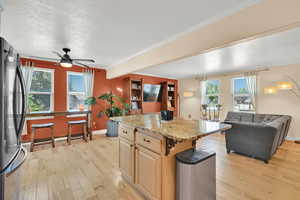 Kitchen featuring freestanding refrigerator, open floor plan, light wood-style floors, a textured ceiling, and baseboards