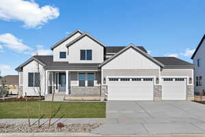 View of front of home with a front yard, covered porch, driveway, an attached garage, and stone siding