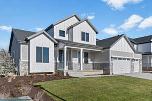 Modern farmhouse with board and batten siding, stone siding, a front lawn, covered porch, and driveway