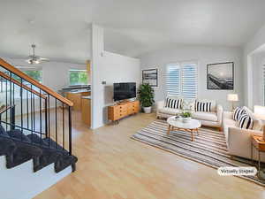 Living area featuring wood finished floors, vaulted ceiling, stairs, a ceiling fan, and baseboards