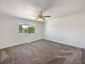 Carpeted spare room featuring a textured ceiling, ceiling fan, baseboards, and crown molding
