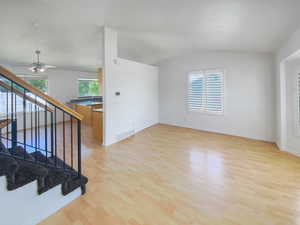 Spare room with light wood-style floors, vaulted ceiling, stairway, a ceiling fan, and baseboards