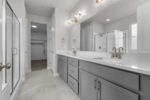 Bathroom featuring marble finish floors, double vanity, a stall shower, a walk in closet, and baseboards