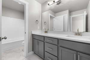 Bathroom with toilet, double vanity, marble look tiles, and baseboards
