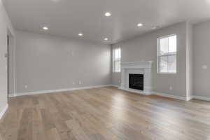 Unfurnished living room with light wood-style flooring, recessed lighting, a glass covered fireplace, and baseboards