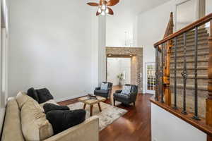 Living room with stairway, a high ceiling, dark wood-type flooring, ceiling fan, and baseboards