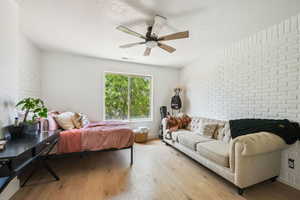 Bedroom with brick wall, hardwood / wood-style flooring, a textured ceiling, and a ceiling fan