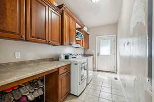 Washroom featuring cabinet space, washing machine and dryer, light tile patterned floors, baseboards, and a textured ceiling