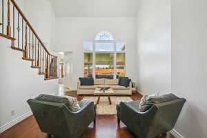 Living room with a high ceiling, dark wood-style flooring, stairs, and baseboards