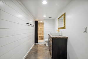 Full bathroom featuring toilet, vanity, wooden walls, concrete flooring, and a stall shower