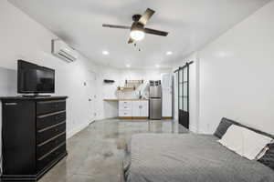 Bedroom featuring a wall mounted AC, freestanding refrigerator, concrete floors, a barn door, and baseboards