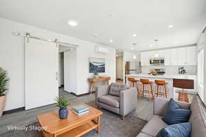 Living room with wood finished floors, a wall mounted AC, a barn door, recessed lighting, and baseboards