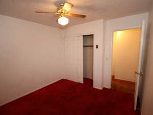 Unfurnished bedroom featuring dark carpet, a closet, baseboards, a ceiling fan, and a textured ceiling
