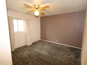 Unfurnished room featuring dark carpet, ceiling fan, and a textured ceiling