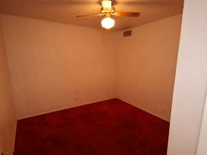 Unfurnished room with a ceiling fan, dark colored carpet, and baseboards