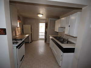 Kitchen featuring white appliances, a sink, light floors, white cabinets, and light countertops