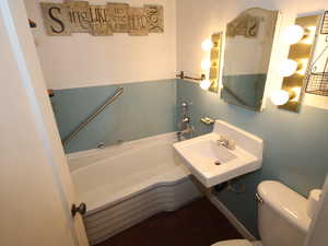 Bathroom featuring a garden tub, toilet, and a sink